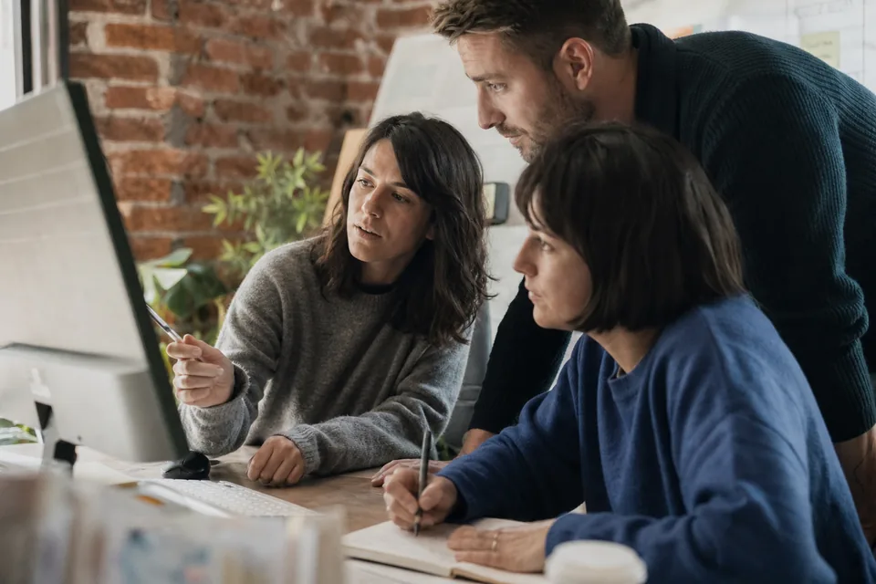 Three person team at a small agency reviewing AI assistant options together around a shared monitor
